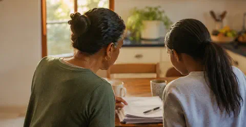 Parent and teenager looking through school reports together at a kitchen table