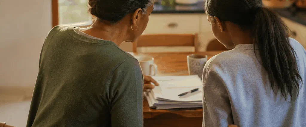 Parent and teenager looking through school reports together at a kitchen table